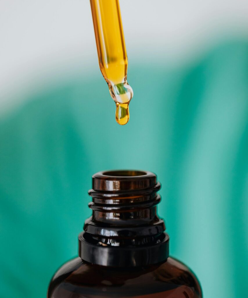 Closeup of anonymous doctor with pipette for fluid dripping yellow medication in brown glass vial while making procedure in clinic